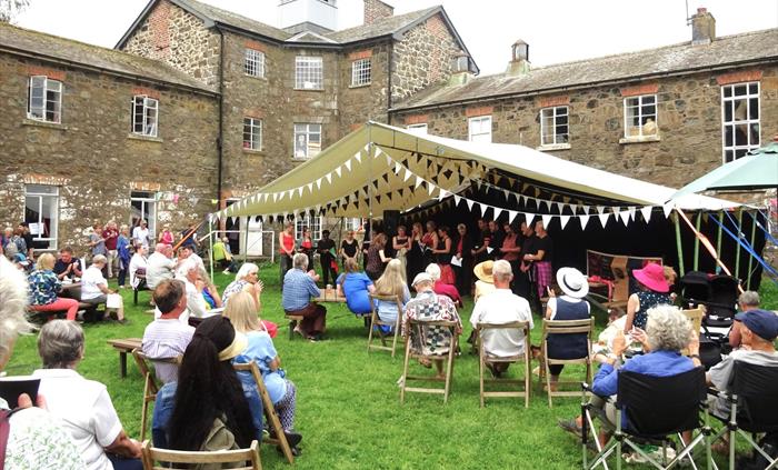 The Vivace Choir performing under a canopy in the Women's Yard at Llanfyllin Workhouse, with an audience sitting on chairs on the lawn.